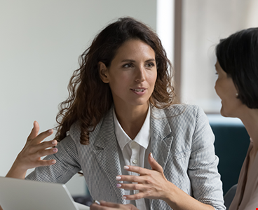 two-business-women-sit-desk-discuss