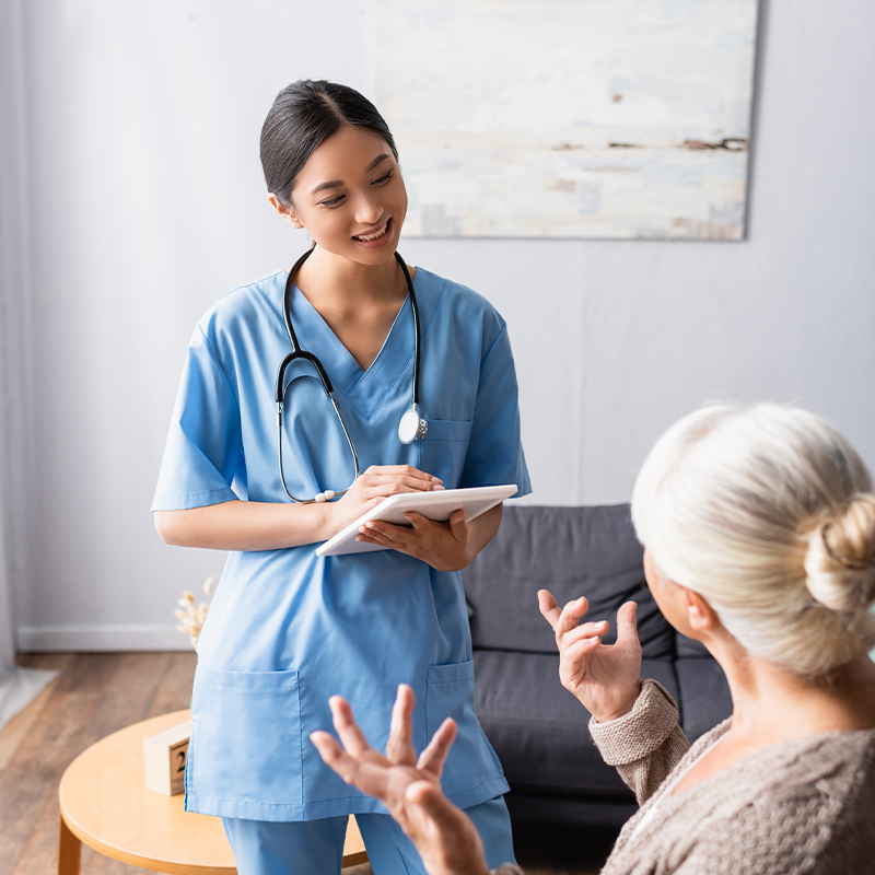 elderly-woman-gesturing-while-talking-to-smiling-asian-nurse-holding-digital-tablet