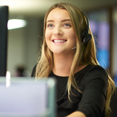 A teenage office worker sits at her desk and speaks on her telephone headset